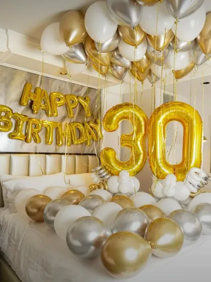 A sophisticated 30th birthday room setup with gold, silver, and white balloons. Large '30' foil balloons make a bold statement over the bed.