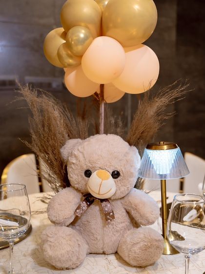A close-up of the adorable teddy bear centerpiece, complete with a small table lamp and balloon bouquet. It's the little details that make the decor feel special.