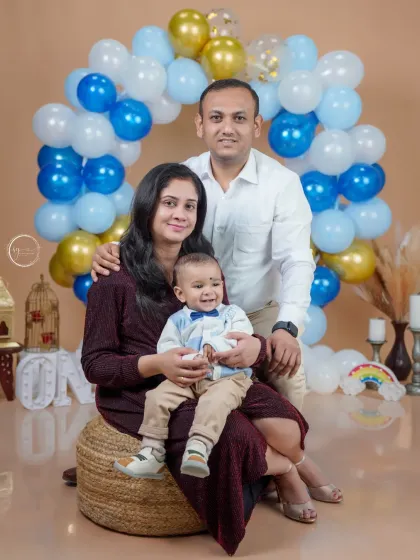 A happy family of three. This studio portrait captures the joy of a young family celebrating their baby's first milestone, surrounded by a festive balloon setup.