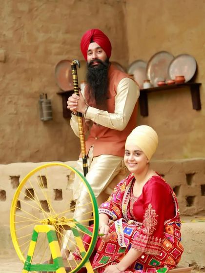 A traditional Punjabi-themed pre-wedding shoot. The couple is dressed in vibrant, traditional attire, complete with a spinning wheel prop, celebrating their cultural roots in a beautiful way.