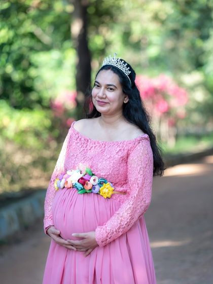 A classic portrait of a mom-to-be in a pink gown and tiara, looking elegant in a park.