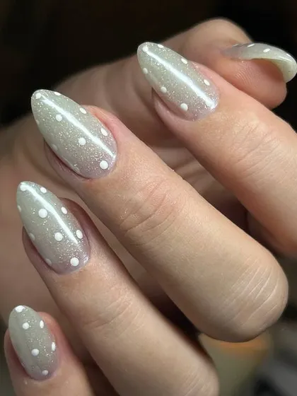 A chic and subtle glitter manicure. This design features a soft, shimmery grey base with delicate white polka dots for a playful yet sophisticated look.