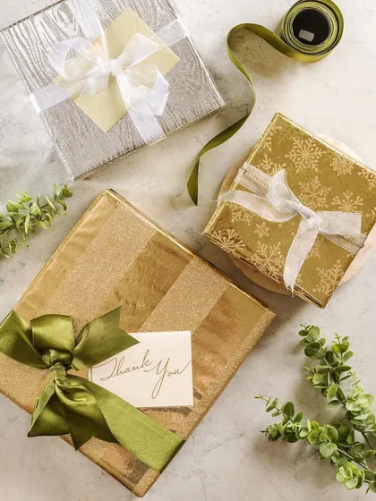 An elegant flat lay of gifts wrapped in gold and green paper from Crown Greetings. The "Thank You" card adds a personal touch, positioning the products as perfect for expressing gratitude.