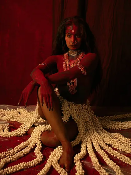 Another image from the 'Kali' series, this time with the model painted in red, symbolizing fury and life force. The composition, with the jasmine skirt spread around her, is both vulnerable and powerful.