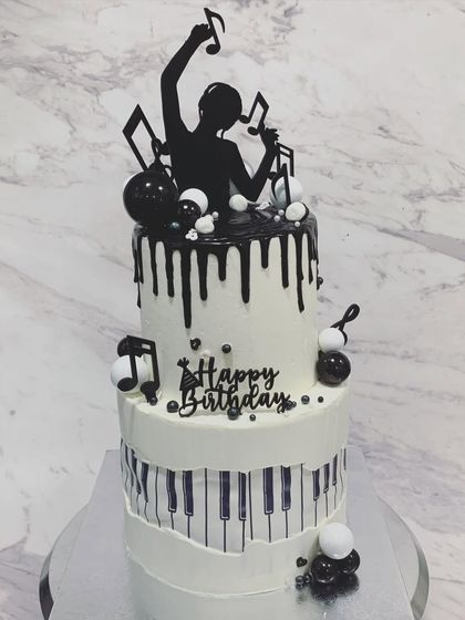 A monochrome music-themed cake for a client who only eats our cakes. This two-tiered design features a piano key wrap, a DJ silhouette topper, and black drip details, making it perfect for any music lover.