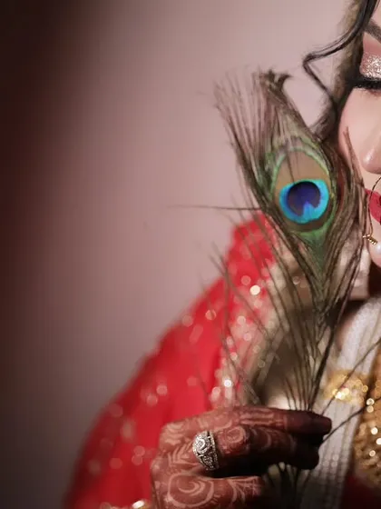 A creative and artistic bridal portrait using a peacock feather as a prop. This close-up shot highlights the bride's flawless makeup and serene expression.