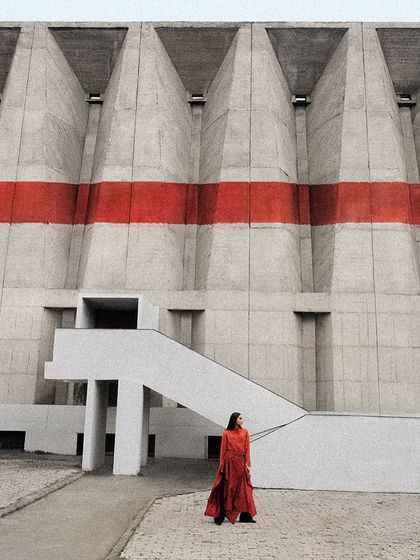 A single figure in a red ensemble stands against a massive concrete structure. This shot for Payal Khandwala emphasizes scale and the power of a single block of color.