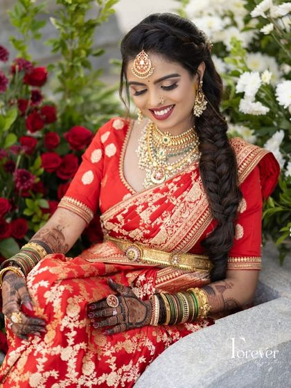A bride seated amidst red roses, her red and gold saree perfectly matching the romantic setting.