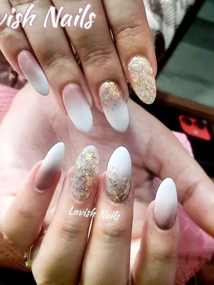 A dramatic ombre nail set blending from nude to white, with accent nails covered in gold foil glitter.