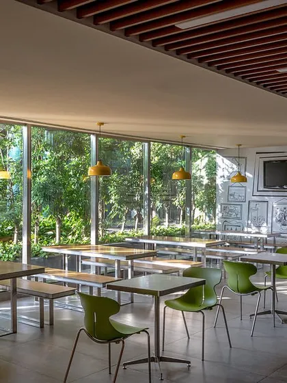 The ground-floor cafeteria is designed with large glass windows overlooking the lush landscape, creating a bright and refreshing space for employees with industrial-style furniture and lighting.