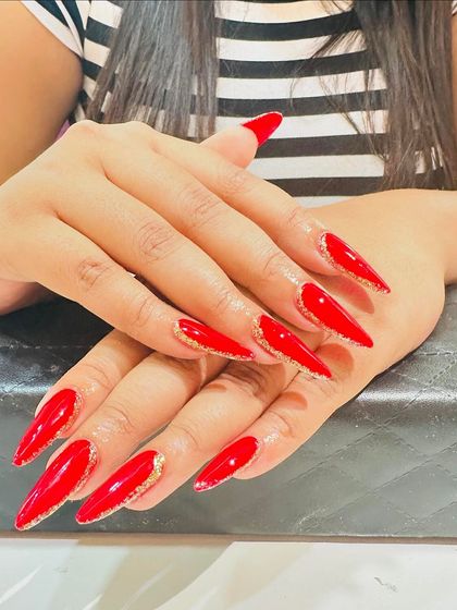 A bold and fiery look with long, stiletto-shaped red nails. A reverse glitter French tip adds a sparkling and modern edge to the design.