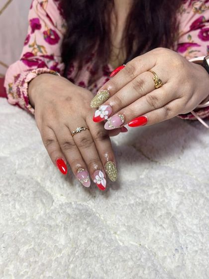 A festive and glamorous set with a mix of solid red, gold glitter, and accent nails with 3D white flowers.