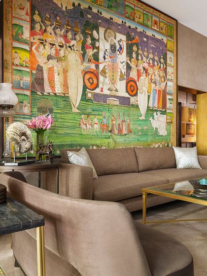The living room in the Courtyard Home is a testament to organic design, where a large pichhwai of Shrinathji from the 1820s hangs above the sofa. The space is filled with collected objects and books, reflecting a life of travel and a deep appreciation for Indian art and culture.