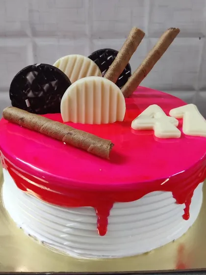A 41st birthday cake with a bright pink glaze and drip effect. It's topped with chocolate wafer rolls and white chocolate decorations.