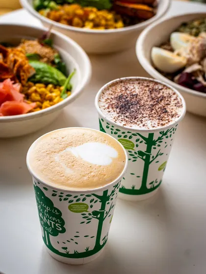 A cozy scene with two coffees and healthy bowls in the background. This image sells not just the food, but the experience of a warm, healthy meal.