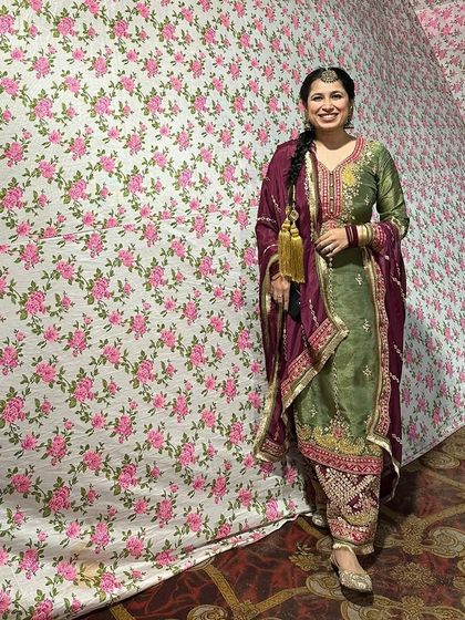 A full portrait of the Punjabi suit look against a floral backdrop. The combination of the embroidered suit, parandi, and juttis is timeless and elegant.