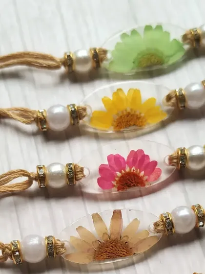 A close-up view of my oval-shaped daisy rakhis. You can see the delicate petals of the real flowers perfectly preserved in the resin. The simple jute thread and pearl accents complete the elegant, earthy look.