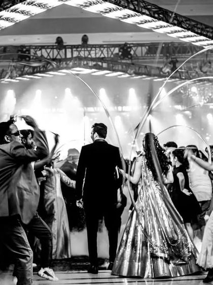 A black and white shot capturing the energy and movement of a grand couple's entry, surrounded by dancers with ribbons.