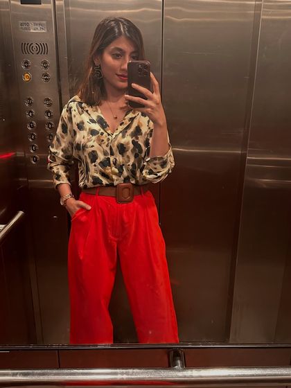 The same red trousers styled with a printed shirt and a wide belt for a bold, confident look captured in an elevator selfie.