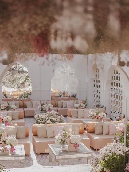 A view from within a guest lounge area, looking out onto the main ceremony space. The design uses layers of jali screens and floral arrangements to create depth and visual interest.