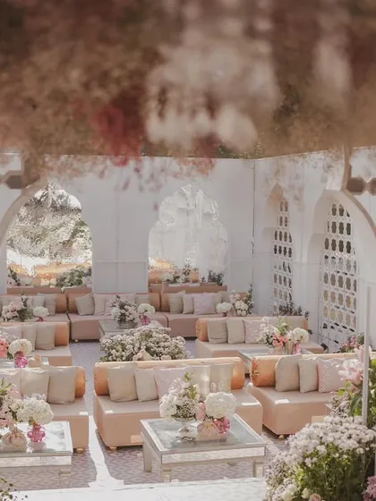 A view from within a guest lounge area, looking out onto the main ceremony space. The design uses layers of jali screens and floral arrangements to create depth and visual interest.