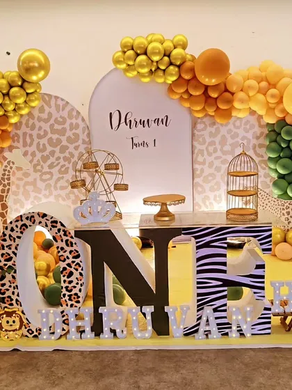 A "Wild One" jungle theme with large 'ONE' marquee letters. This setup features animal-print letters, character cutouts, and a rich orange and green balloon arch.