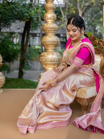 A bride seated on a golden chair, looking like royalty in her cream and pink silk saree. The blouse features delicate embroidery that adds to the overall elegance.