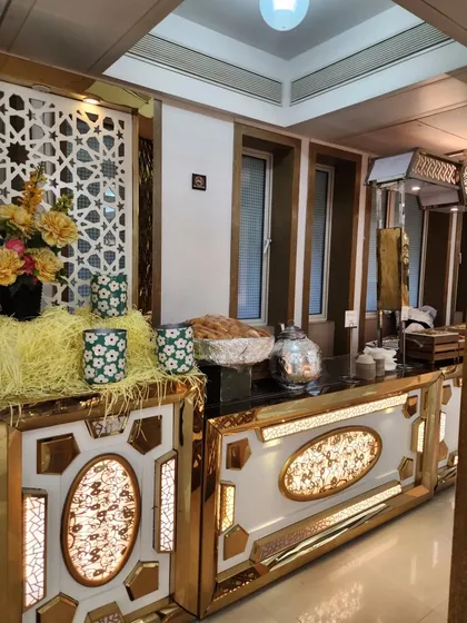 An elegant buffet counter with intricate gold and white designs, decorated with floral arrangements. This kind of setup is ideal for high end weddings and festive celebrations.