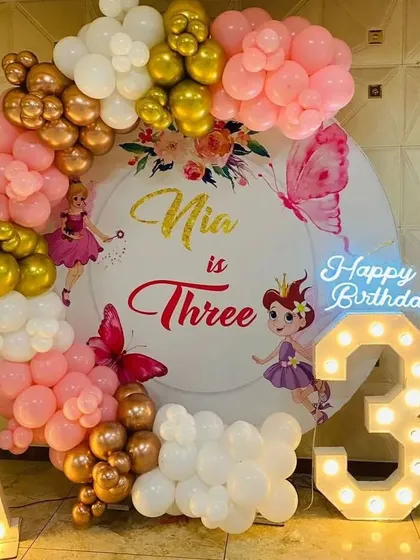 A fairy-themed 3rd birthday party. This decoration features a personalized backdrop, a pink and gold balloon arch, and marquee letters and numbers.