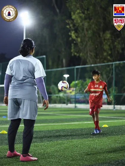 A female coach guides a young player through a ball control drill. We provide expert mentorship for all our athletes, ensuring personalized attention.