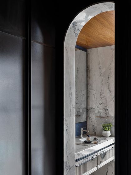 An arched doorway frames the view into the master bathroom, revealing a space of luxurious serenity. The combination of Calacutta marble, a wood-paneled ceiling, and handcrafted stonework transforms the ensuite into a private oasis.