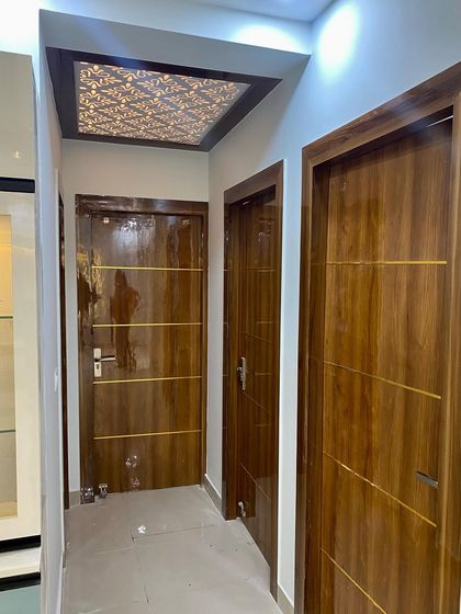A view of a hallway with matching wooden flush doors featuring gold inlay work, and a foyer ceiling with a beautiful jali panel.
