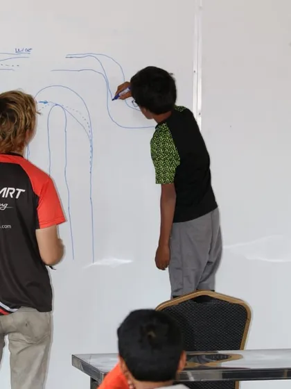 Victory is engineered through strategy and knowledge. Here, one of our senior coaches works with a young academy driver, breaking down the racing line on a whiteboard. This theoretical instruction is a crucial part of our comprehensive driver development program.