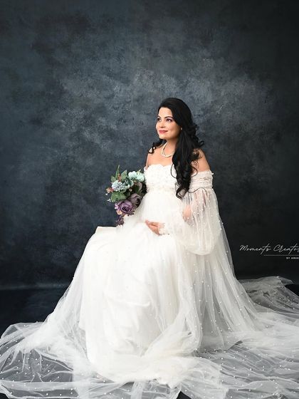 A classic seated portrait. The mom-to-be holds a bouquet, looking off to the side with a graceful and thoughtful expression.