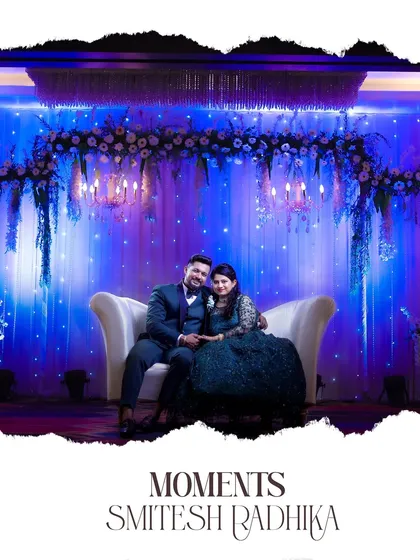 A stunning reception portrait of a couple on a white couch, set against a dramatic blue and purple floral backdrop.
