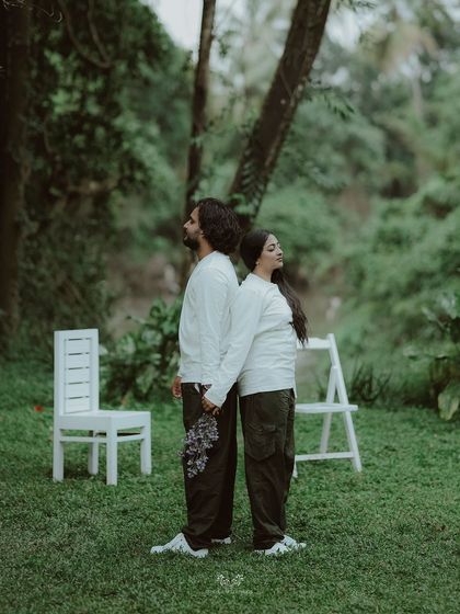 A minimalist and artistic shot of a couple standing back-to-back, holding hands in a green field.