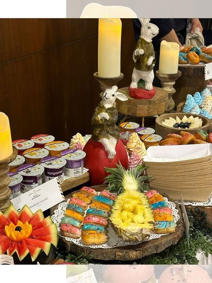 A colourful and fun dessert section of a grazing table, showcasing rainbow donuts, fresh fruit carved into fun shapes, and individual yogurt cups.