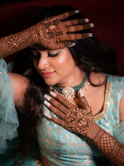 Fun and candid moments from a mehendi ceremony. The bride's makeup is fresh and playful, with a winged liner and glowing skin, perfect for celebrating with her loved ones. The hairstyle is a soft half-updo with pretty accessories.