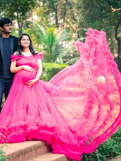 The ruffled pink gown creates a stunning visual effect as it spreads out, framing the happy couple in this garden portrait.