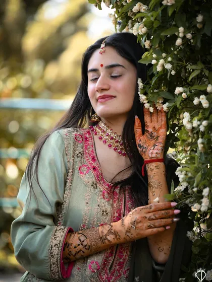 A serene portrait of the bride with her eyes closed, surrounded by white flowers, showcasing the beautiful henna art on her hands.