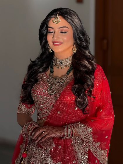 A beautiful bride in a stunning red lehenga, perfect for a reception. The makeup is glamorous, with soft waves and a radiant complexion.