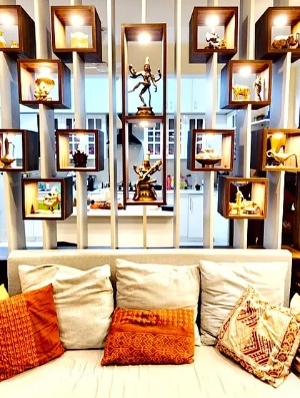 A living room partition made of illuminated wooden boxes displaying traditional Indian brass artifacts like the Nataraja statue.