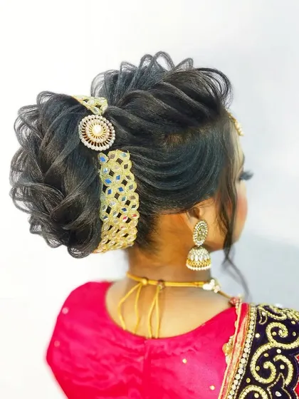 A textured, messy bun accessorized with a broad, traditional hairpiece. This style is perfect for guests who want a fashionable yet classic look for a wedding event.
