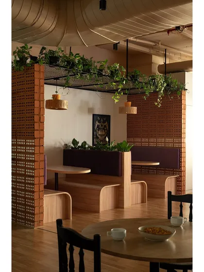 In a busy office, creating zones for quiet work or leisure is key. This seating niche uses raw hollow bricks and an overhead mesh for plants, blending an industrial vibe with biophilic design to create a refreshing breakout area.