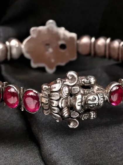 A detailed shot of the handcrafted silver bracelet, focusing on the seated goddess Lakshmi motif and the surrounding red stones.