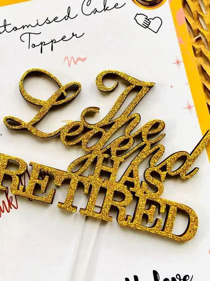 A close-up of "The Legend Has Retired" topper, showing the texture and sparkle of the gold glitter.