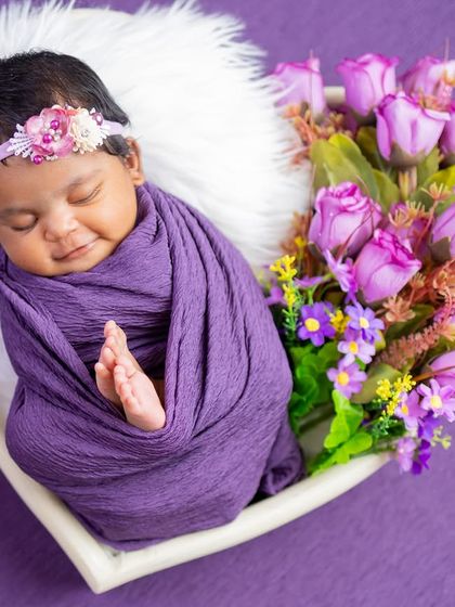 A sweet sleeping smile from this baby, swaddled in purple and surrounded by matching flowers. This is a perfect example of a color-coordinated, beautiful setup.