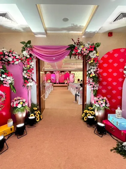 A bright and cheerful entrance for a Haldi ceremony, using a fun flamingo motif, vibrant pink and red panels, and lush floral arrangements to create a tropical and festive vibe.
