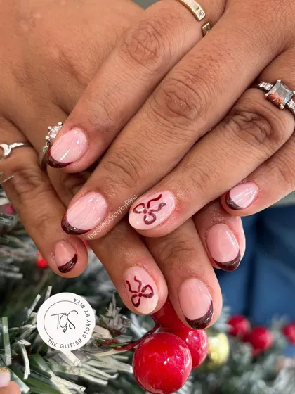 A cute and festive Christmas-themed French manicure. This set features deep red-brown tips with hand-painted bow accents on a sheer pink base.