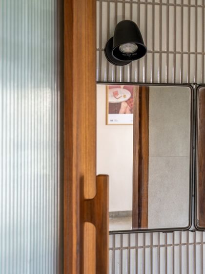 A detail of the bathroom, where a custom wooden door handle and simple black light fixture complement the textured vertical tiles. Every element is chosen to contribute to the home's narrative.